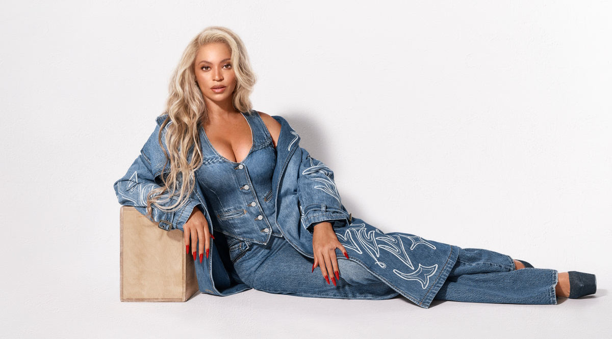 Marka Levi’s® ponownie łączy siły z Beyoncé, prezentując drugi rozdział kampanii REIIMAGINE. Beyoncé w dżinsowym komplecie siedzi na podłodze, opierając się o prostokątna skrzynkę.
