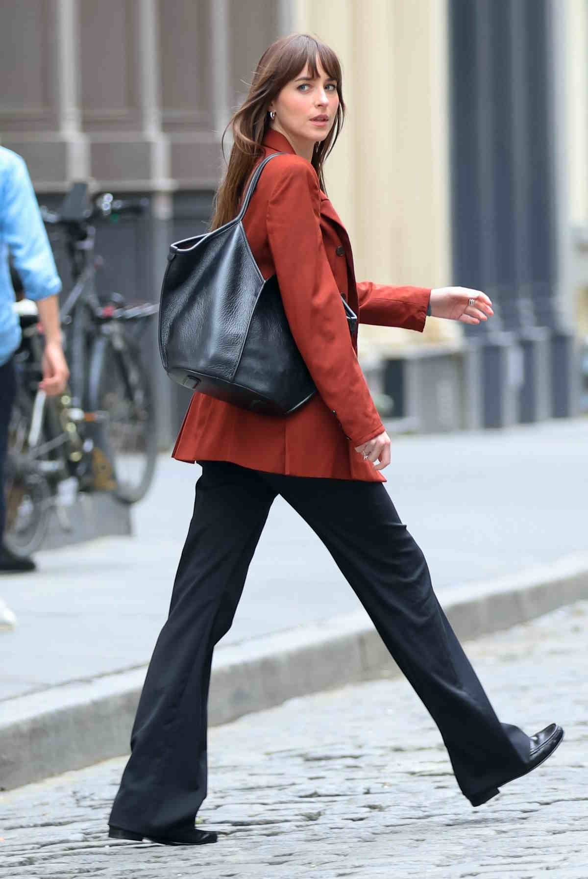Ikona stylu Dakota Johnson znalazła idealną czarną torbę shopper. Stylizuje pomarańczową marynarkę, czarne spodnie i czarne mokasyny.
