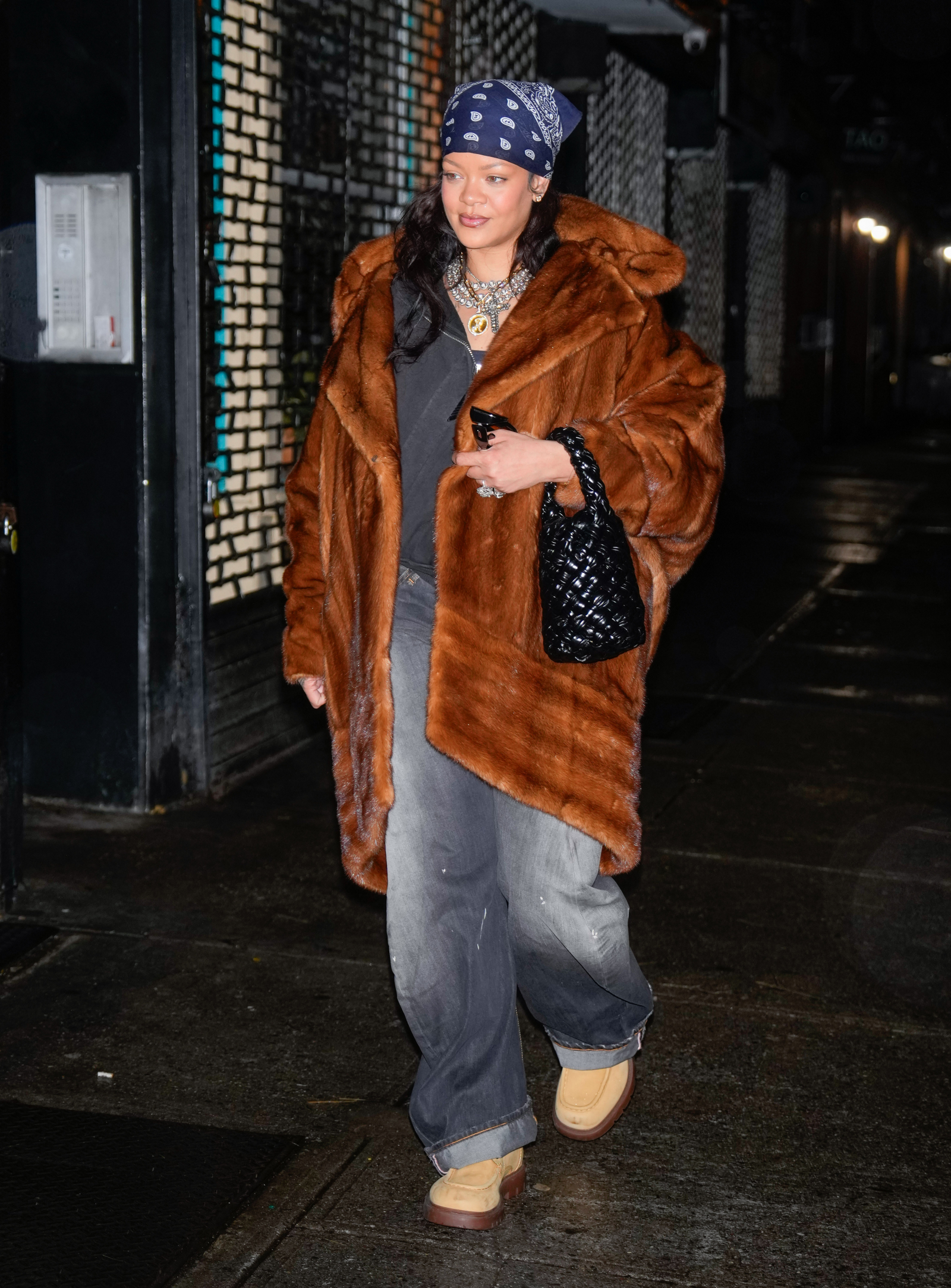 Rihanna w brązowym futrze, zamszowych traperach i chustce na głowie, spaceruje po ulicy.