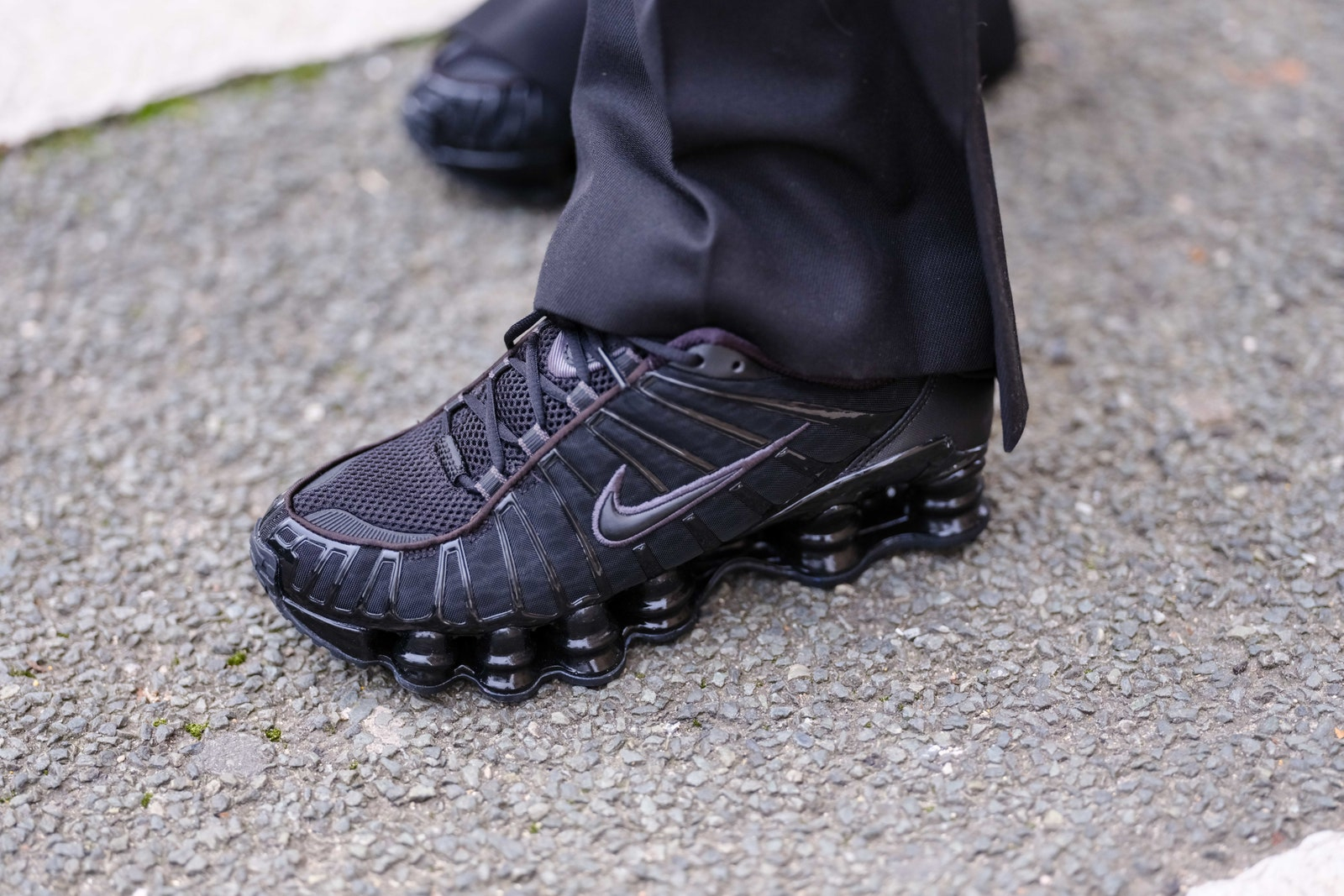 Damskie sneakersy Nike Shox w kolorze czarnym, z charakterystycznymi sprężystymi podeszwami, na szarej nawierzchni.