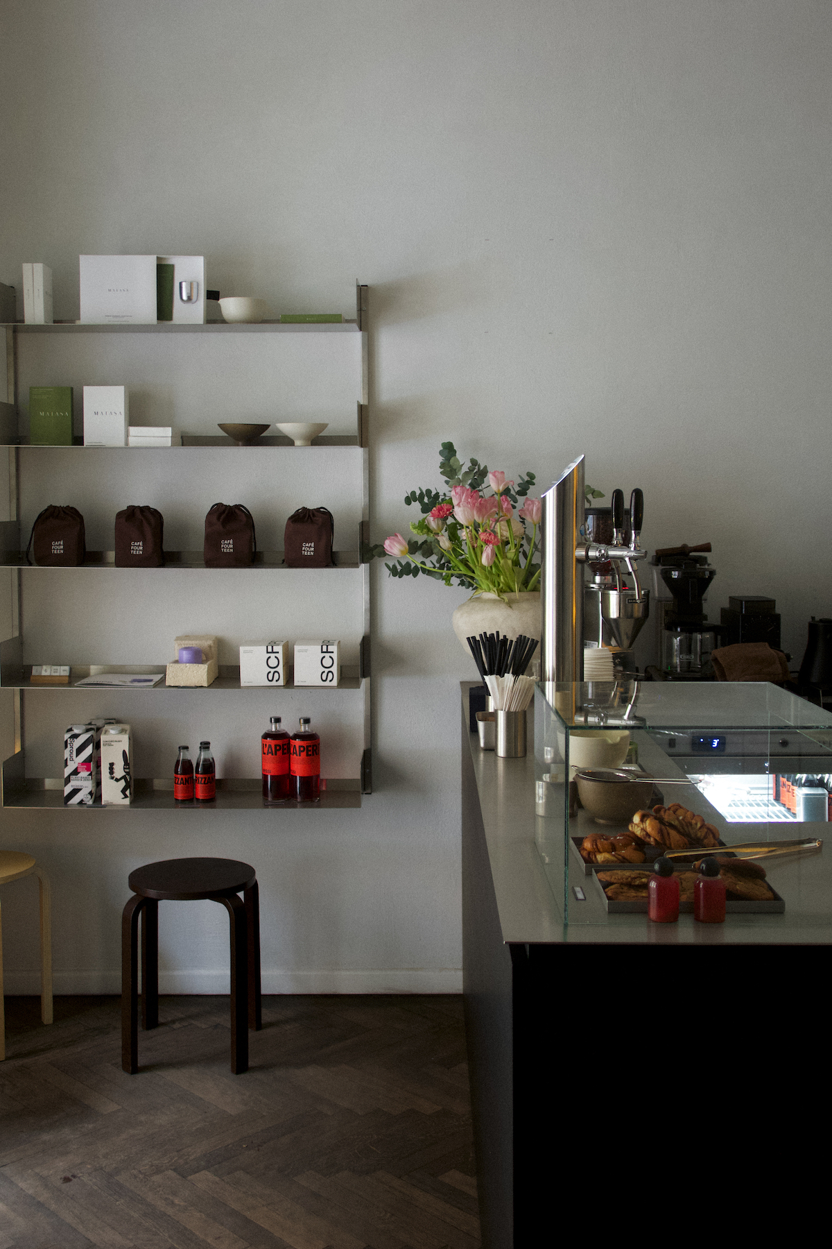 Stylowe wnętrze kawiarni Café Fourteen w Warszawie z półkami pełnymi produktów, kwiatami i ekspresami do kawy.
