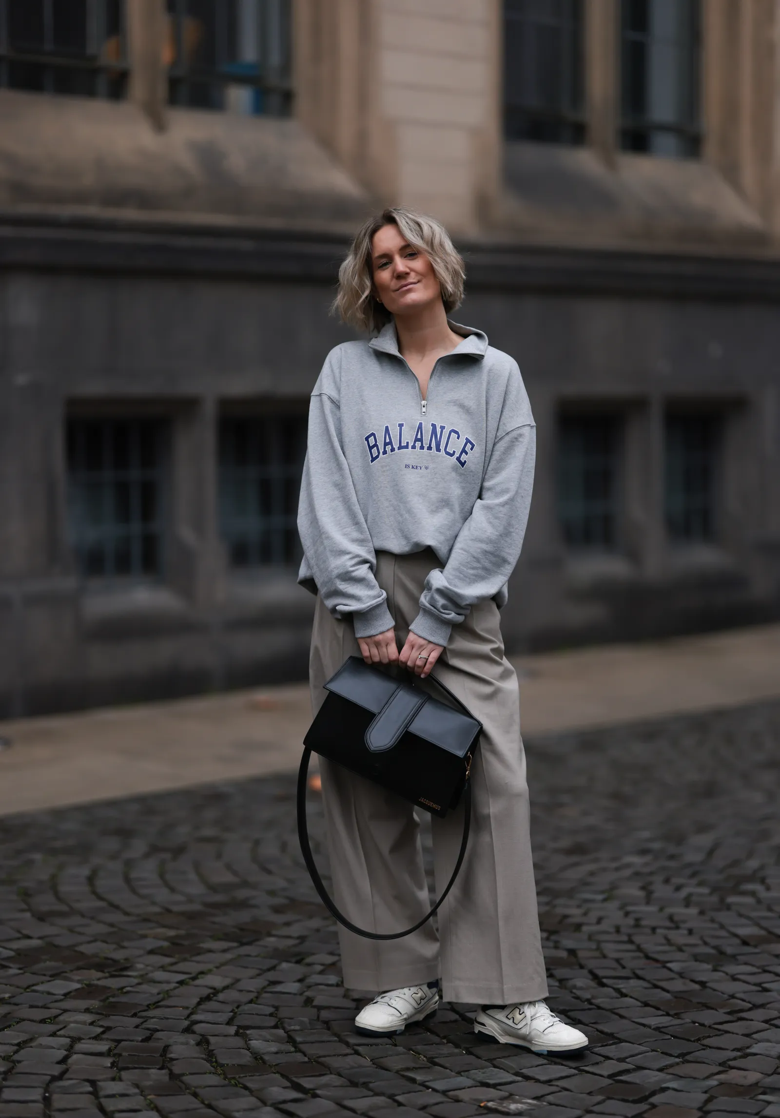 Kobieta w szarej bluzie, eleganckich spodniach i białych sneakersach