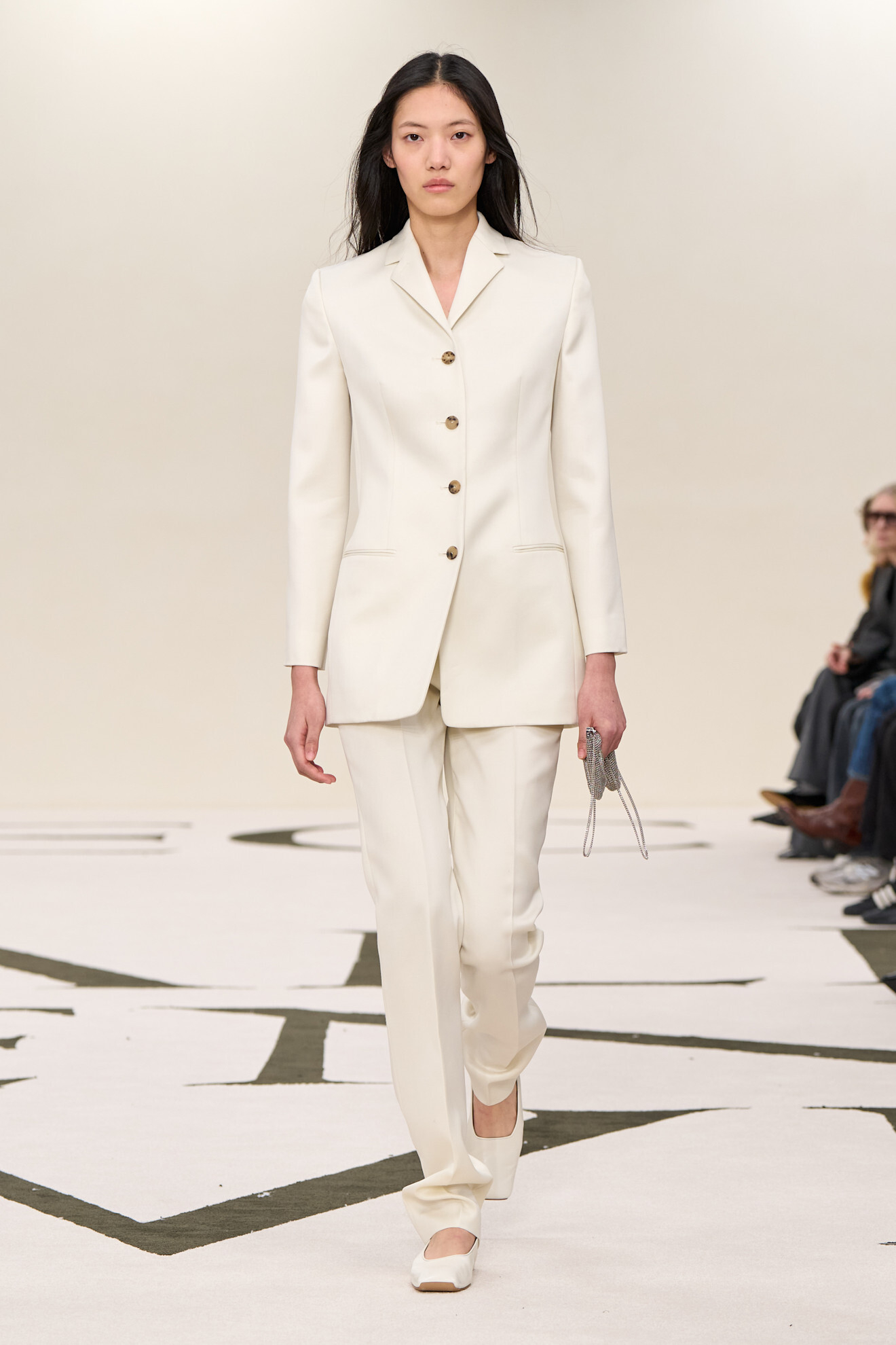Modelka w eleganckim, białym garniturze od Calvin Klein na wybiegu, przechodzi przed widownią.