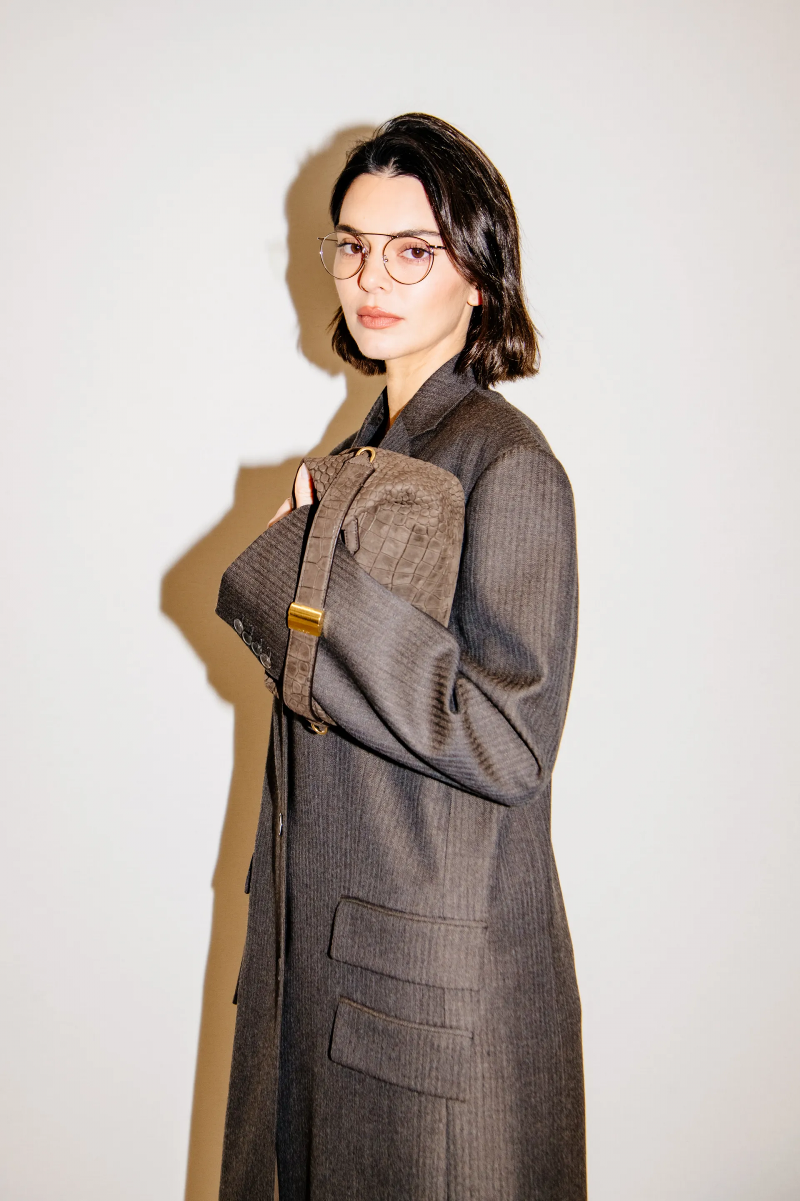Kendall Jenner w eleganckim płaszczu i okularach, trzyma torbę od Calvin Klein.