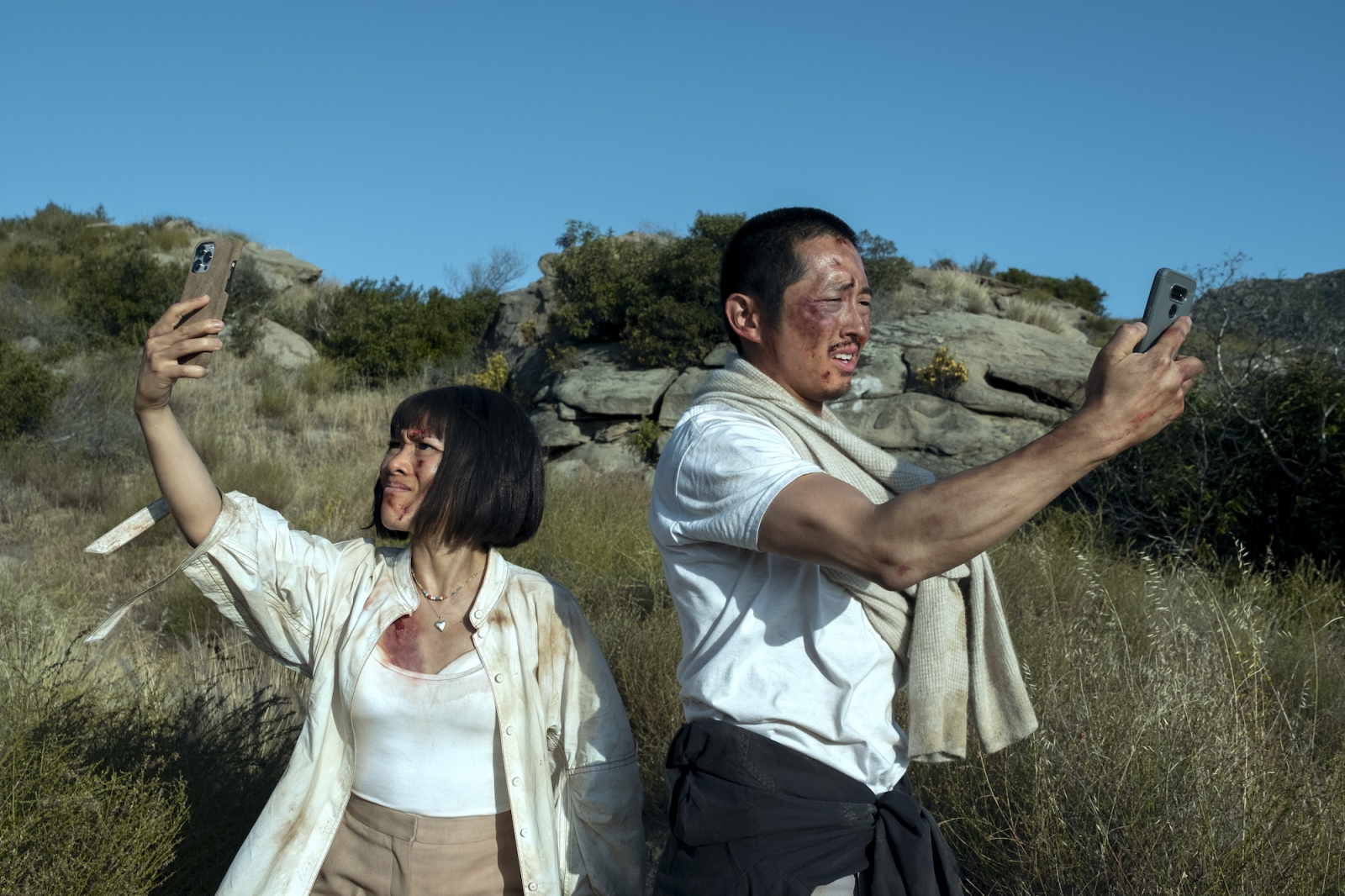 Ali Wong i Steven Yeun w scenie z serialu Netflix „Awantura”, pozują w zniszczonych ubraniach na tle natury.