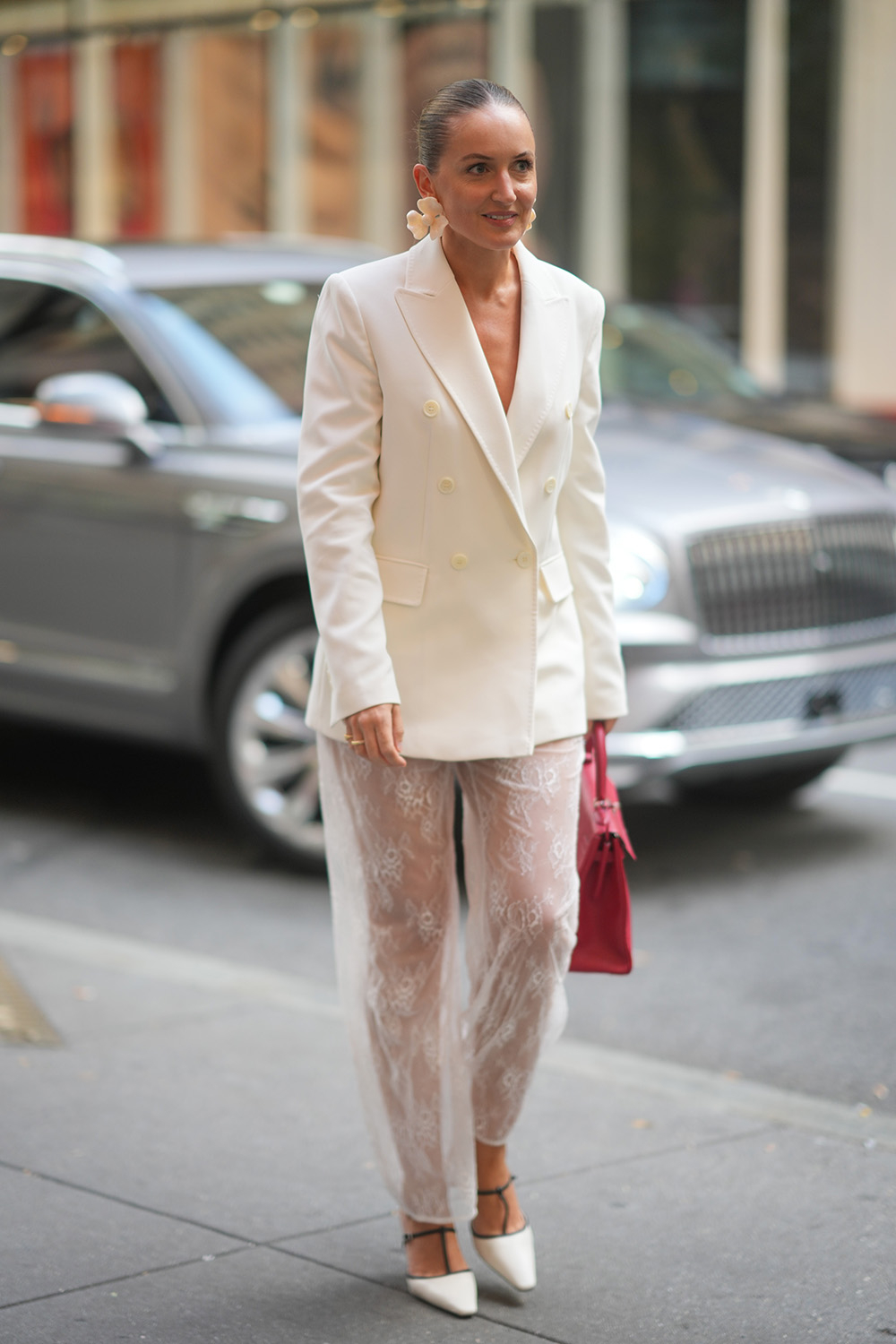 Kobieta w białej, koronkowej spodniach i eleganckim żakiecie w stylu boho, trzyma torebkę w intensywnym kolorze.