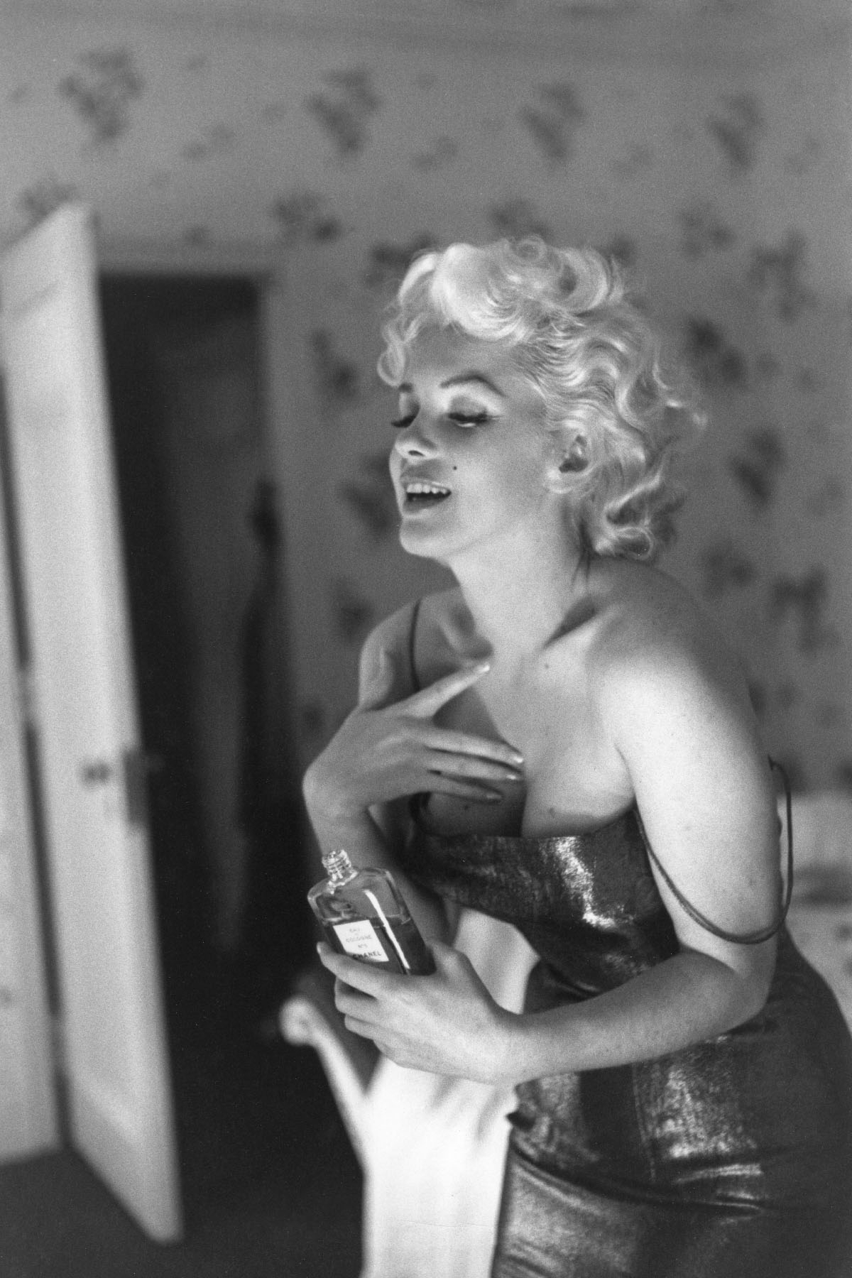 Marilyn Monroe aplikuje perfumy Chanel No. 5, uśmiechając się w eleganckiej, błyszczącej sukience.