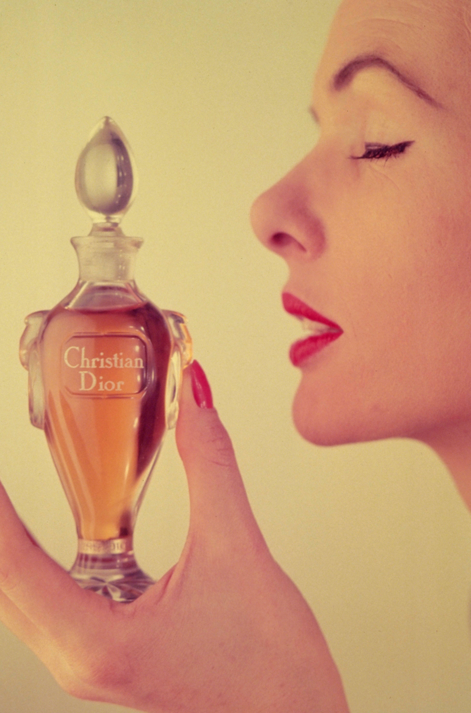 Modelka na retro zdjęciu trzyma flakon perfum Miss Dior, delikatnie wąchając zapach.