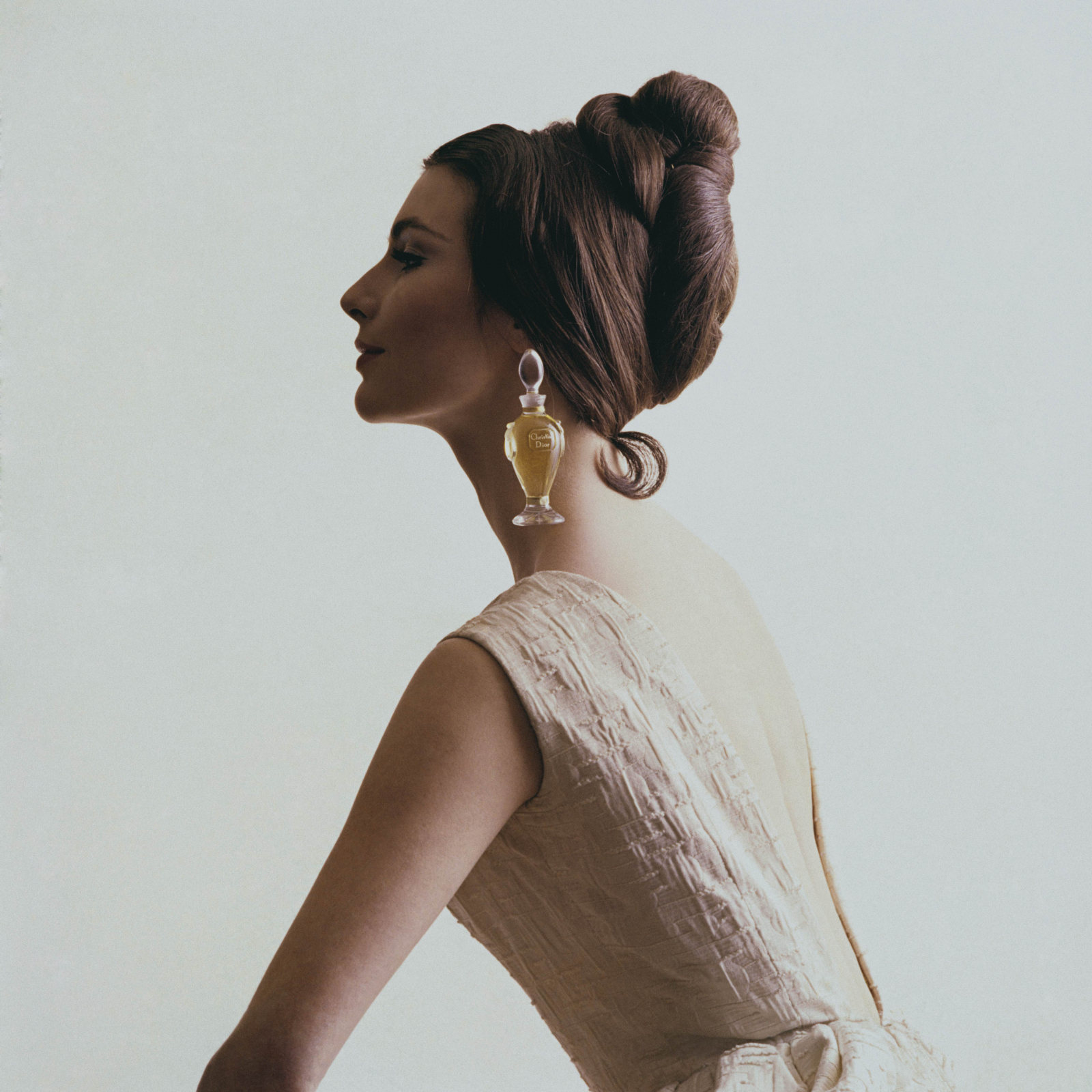 Kobieta w eleganckiej sukni z wysokim upięciem włosów, nosi perfumy Dior. Fotografia z magazynu Vogue.