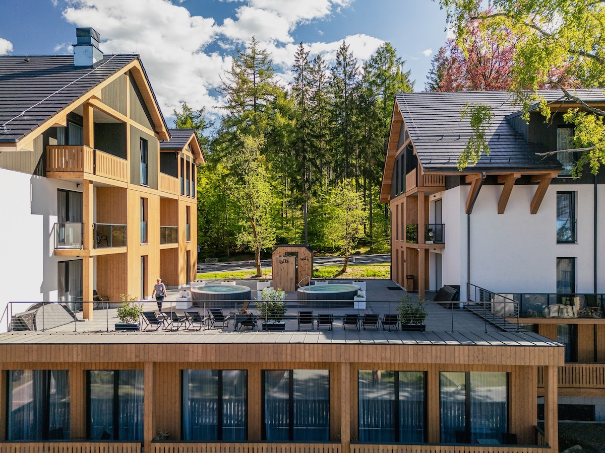 Nowoczesne budynki hotelowe Aqua by Grano w Szklarskiej Porębie z drewnianymi detalami, jacuzzi na tarasie, w otoczeniu zieleni i drzew. 