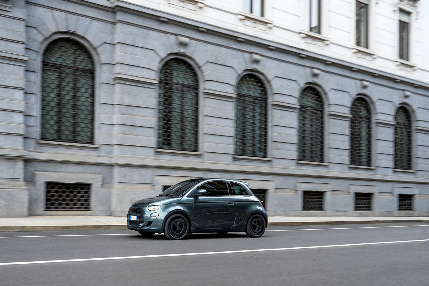 Samochód Fiat 500e Giorgio Armani w kolorze ciemnozielonym jedzie po ulicy Mediolanu.