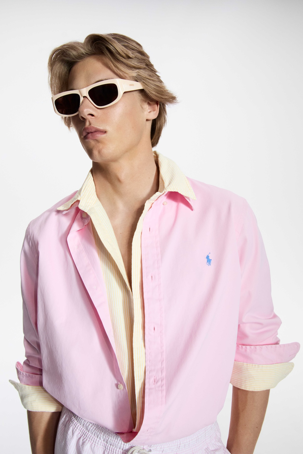 Model w różowej i żółtej koszuli marki Ralph Lauren, noszący okulary przeciwsłoneczne.