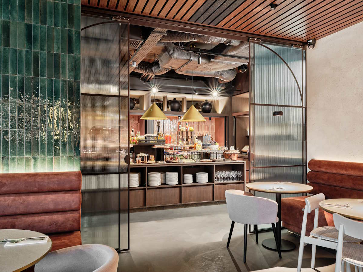 Nowoczesne wnętrze restauracji Mövenpick Resort & Spa Karpacz z widokiem na bar, brązowe sofy i okrągłe stoły, zielone płytki na ścianie.