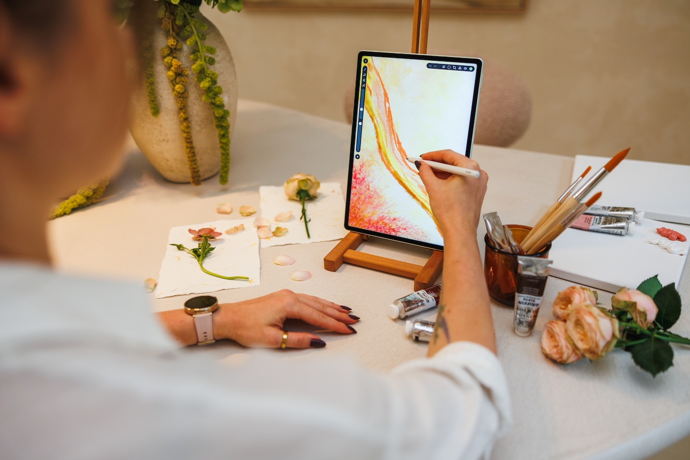 Osoba korzysta z tabletu Huawei MatePad Pro, malując na ekranie w artystycznym otoczeniu pełnym pędzli, farb i kwiatów.