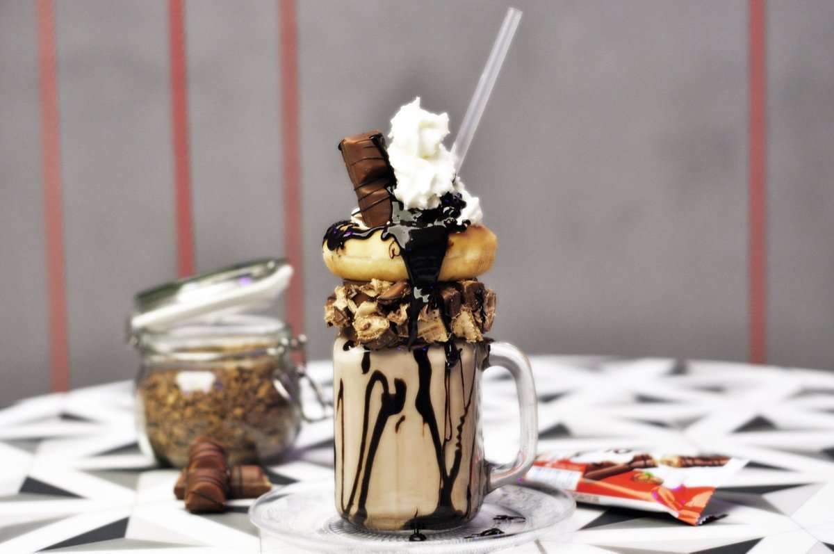 Propozycja mlecznego koktajlu z cukierni Warszawski Lukier. Piętrowy shake z dodatkiem pączka, batonika Kinder Bueno i polewy czekoladowej.
