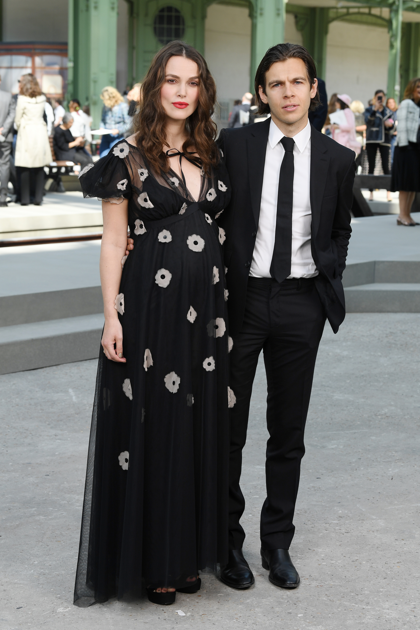 Keira Knightley w czarnej sukni w kwiaty z Jamesem Rightonem, oboje pozują na tle eleganckiego wydarzenia w 2020 roku.