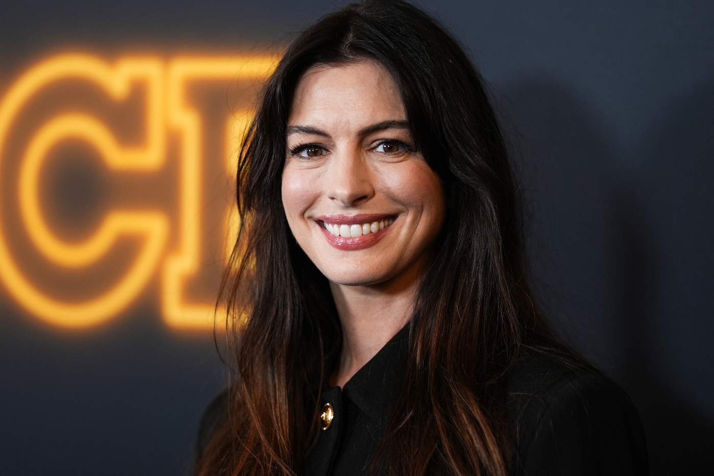 Anne Hathaway w czarnej marynarce i długich, rozpuszczonych włosach.