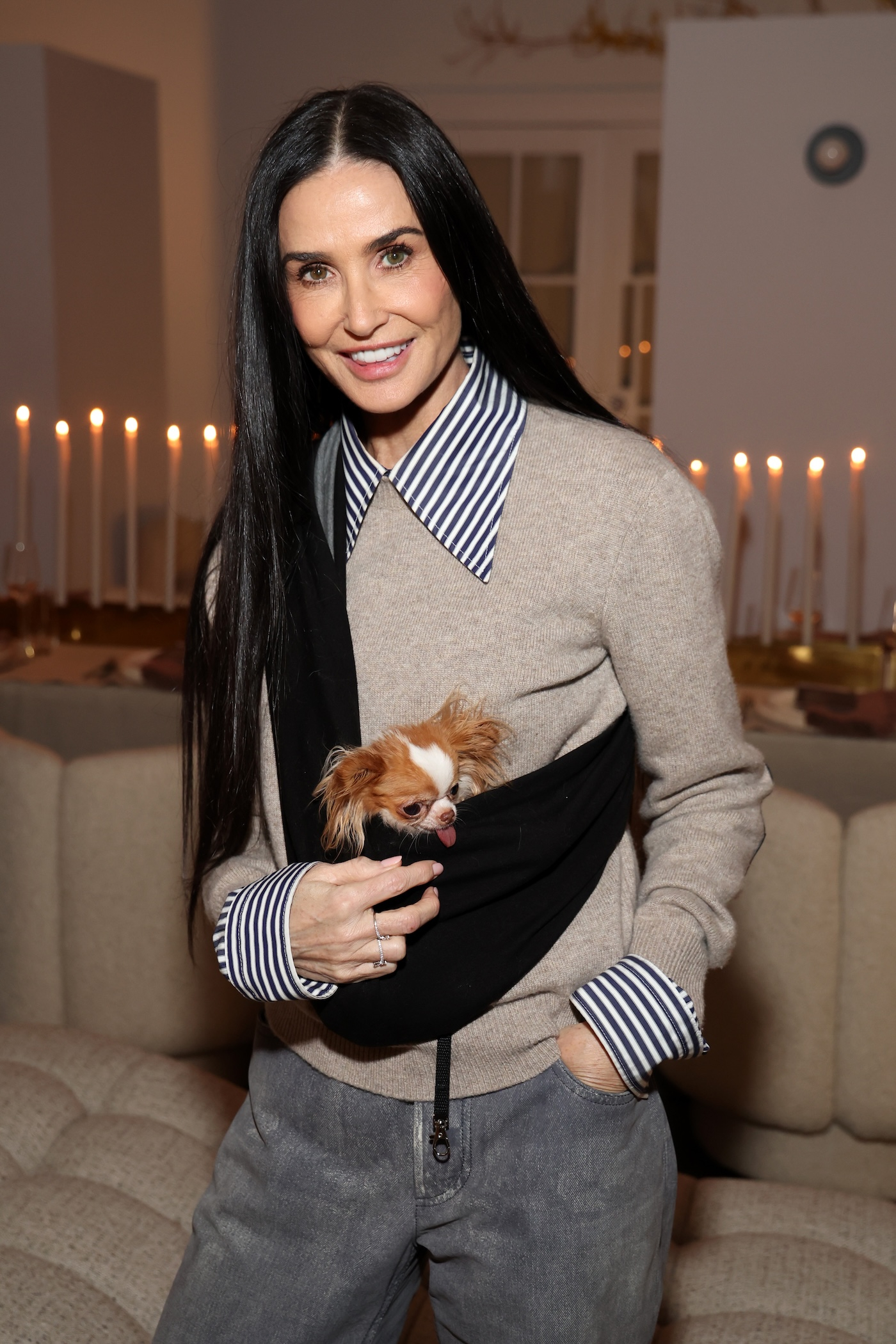 Demi Moore nosi szare jeansy z prostą, ale za długą nogawką, beżowy casualowy sweterek, koszulę w paski z przeskalowanym kołnierzykiem i mankietami oraz torebkę-nerkę, w której trzyma swojego pieska Pilafa.