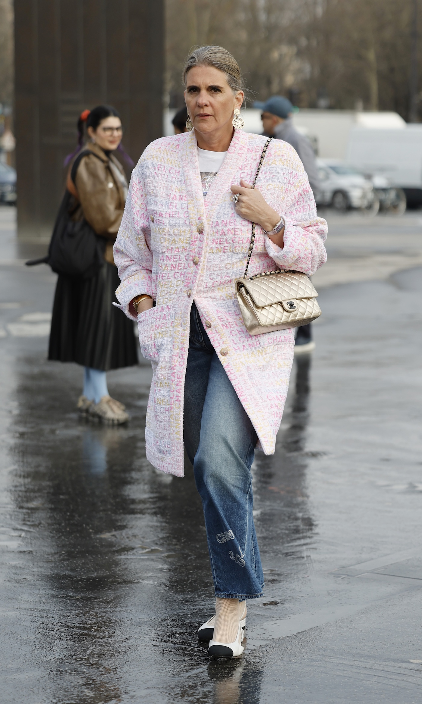 Kobieta sfotografowana podczas Paris Fashion Week, ma na sobie dwukolorowe buty, pastelowy ozdobny kardigan Chanel, błękitne jeasny oraz białą pikowaną torebkę Chanel na łańcuszku.