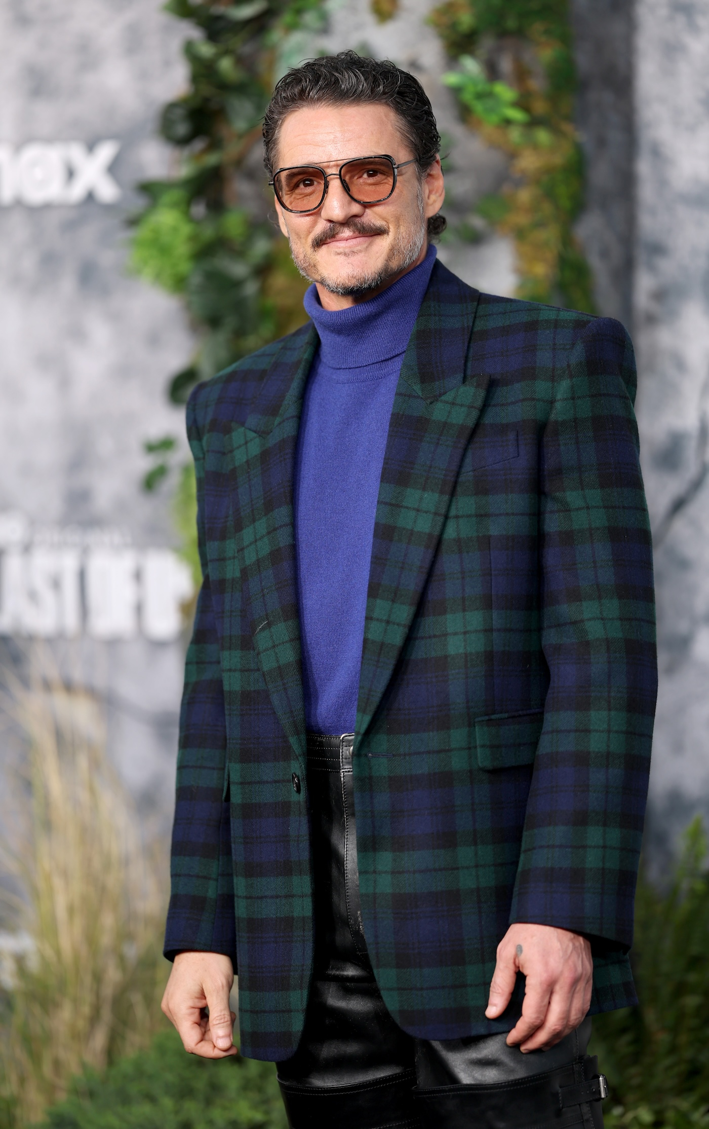 Pedro Pascal na premierze 2 sezonu serialu "The Last of Us" ma na sobie retro okulary z pomarańczowymi szkłami, golf w kolorze ultramaryny i marynarkę w kratę typu tartan.